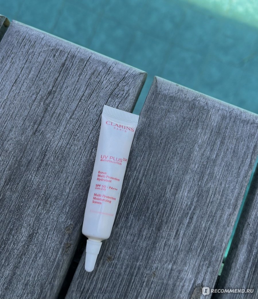Clarins UV Plus Anti-Pollution SPF 50 — маленький тюбик флюида на деревянной поверхности у бассейна