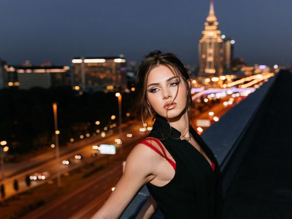 Девушка на крыше на фоне вечерней Москвы: тёмно-русые волосы собраны в небрежный низкий пучок с прядями у лица, графичная чёрная стрелка — макияж для фотосессии